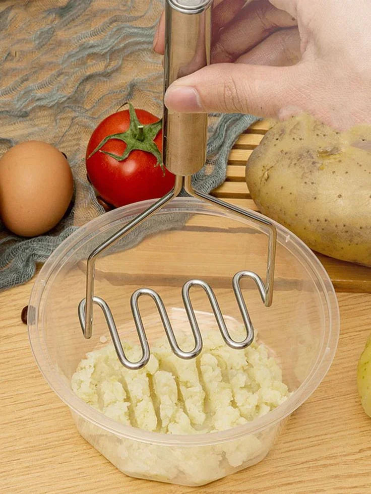 Stainless steel potato masher mashing potatoes in a bowl with food ingredients nearby