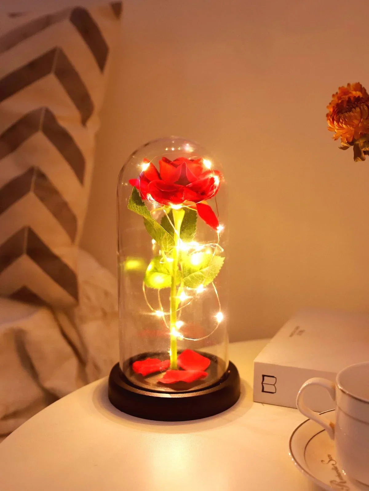 Red rose in glass dome with LED fairy lights on nightstand, cozy decor