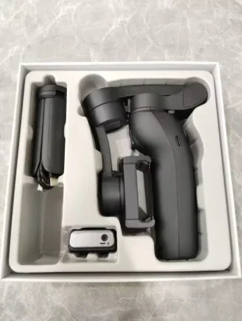 Black handheld camera gimbal stabilizer set in foam packaging, on a marble surface