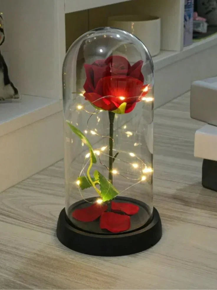 Red artificial rose under glass dome with LED fairy lights on wooden table, decorative gift